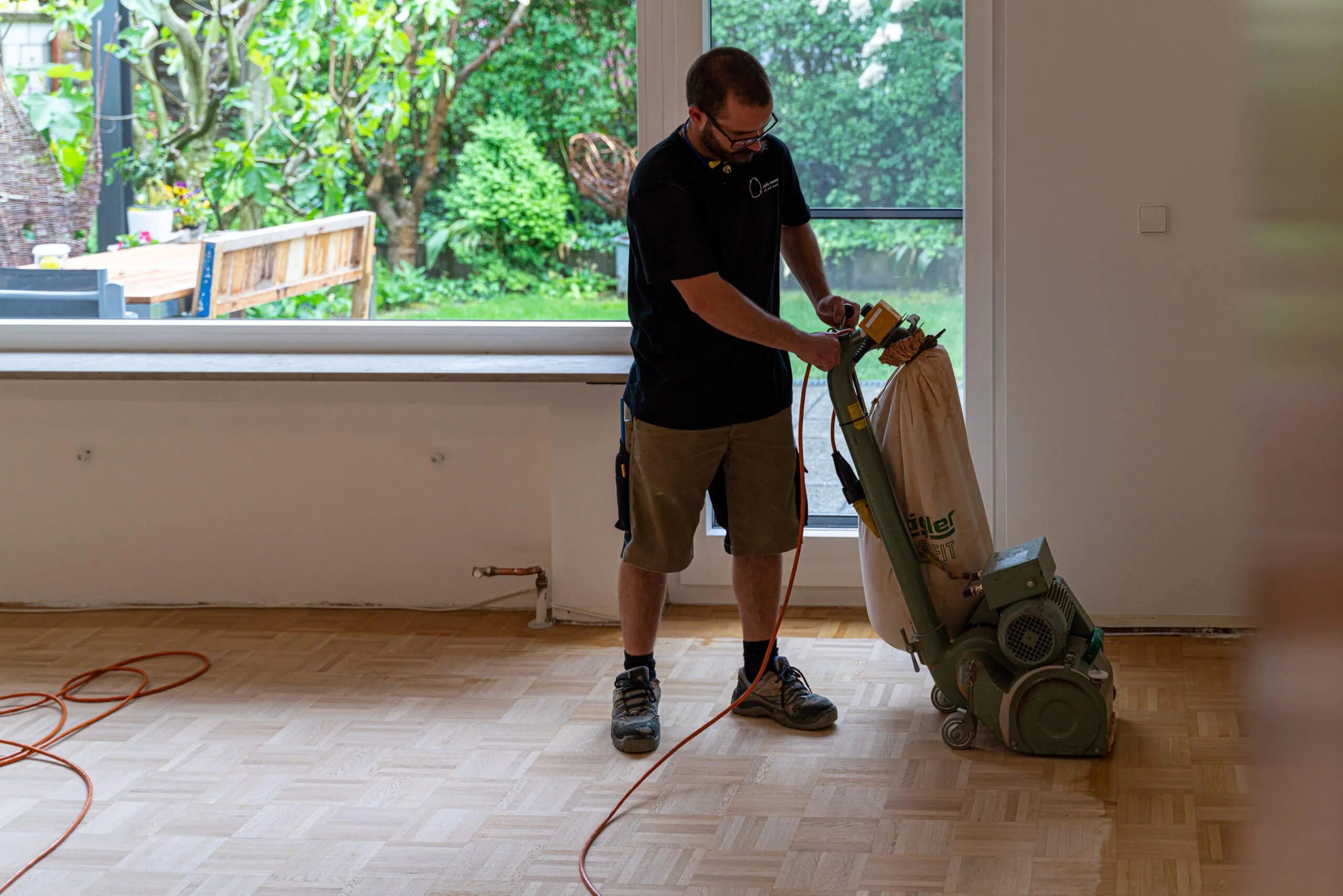Ein Handwerker schleift mit einer Maschine einen Parkettboden in einem hellen Raum