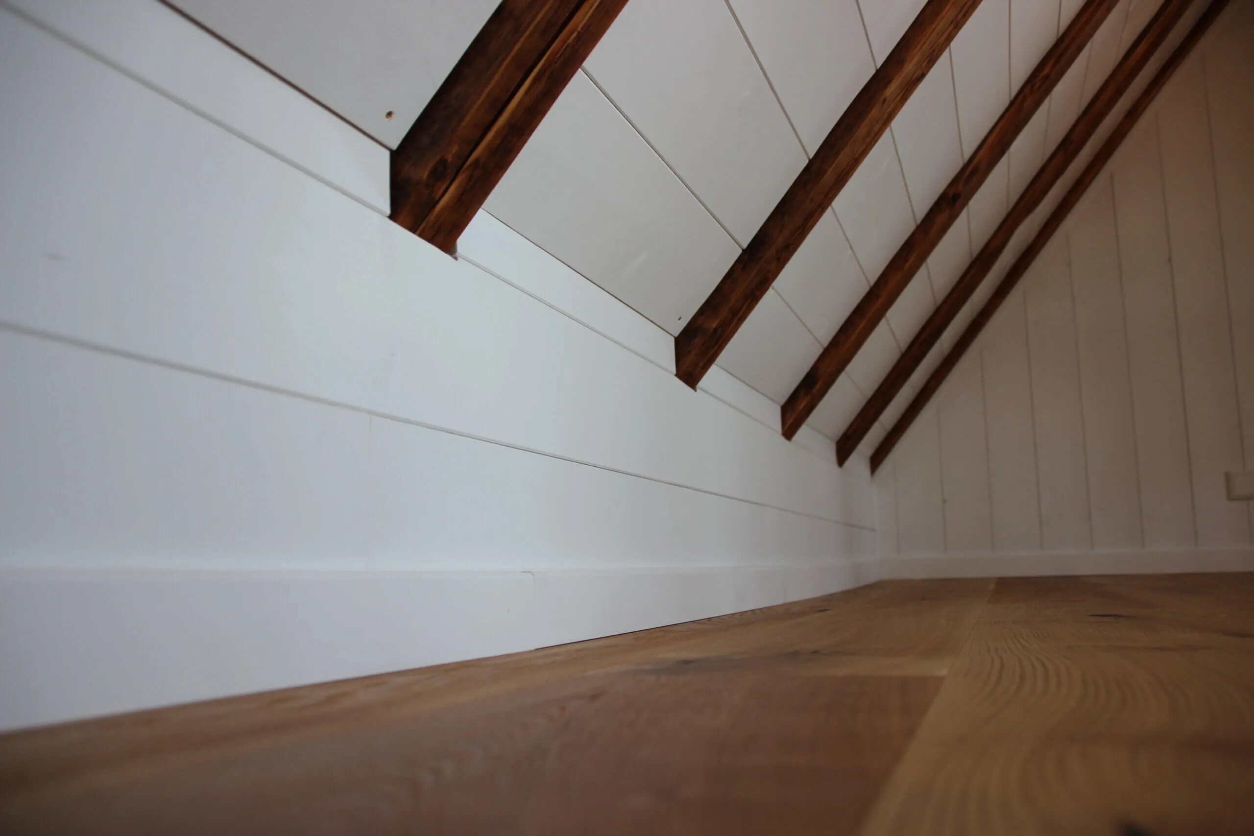 Ausgebaute Dachschräge mit weißer Verkleidung, Holzbalken und Dielenboden
